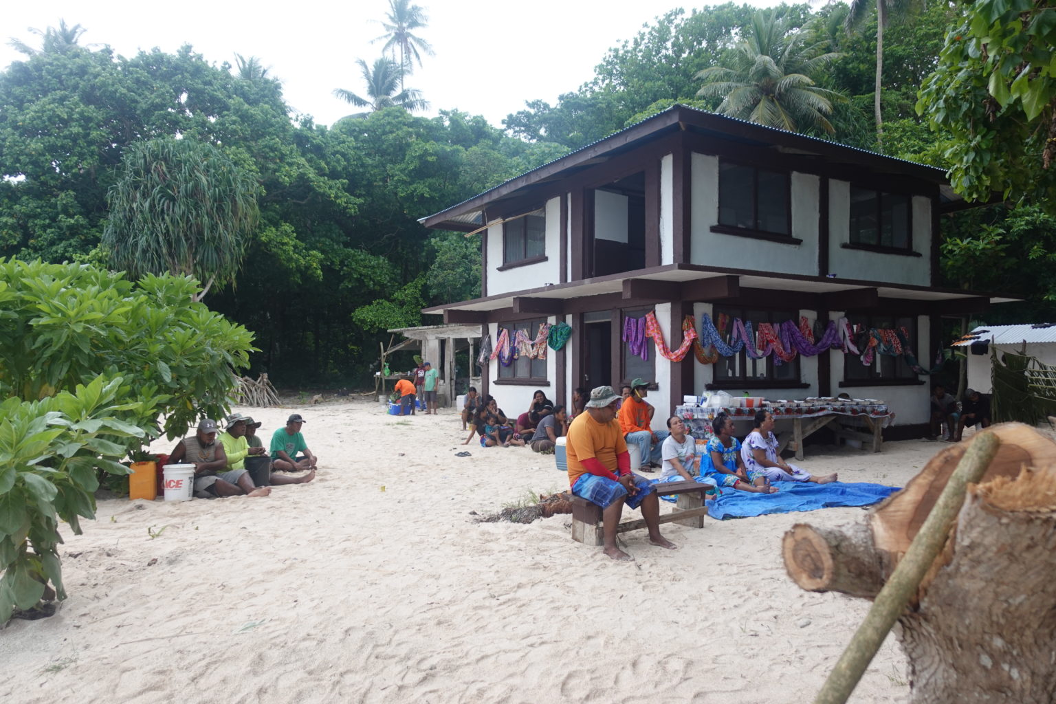 Pacific islanders sit on benches in front ofuilding on beach