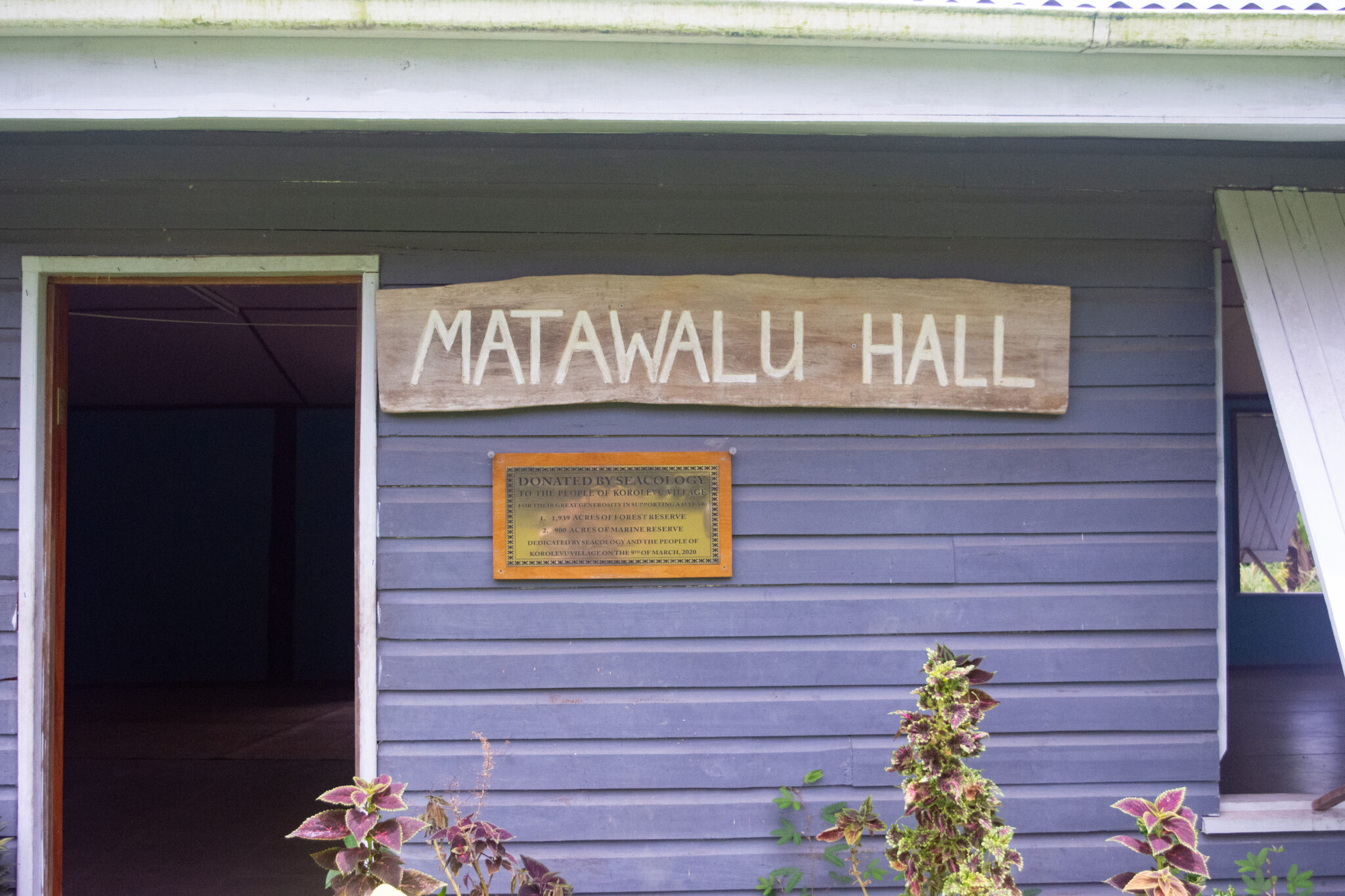 front of community hall with sign and dedication plaque