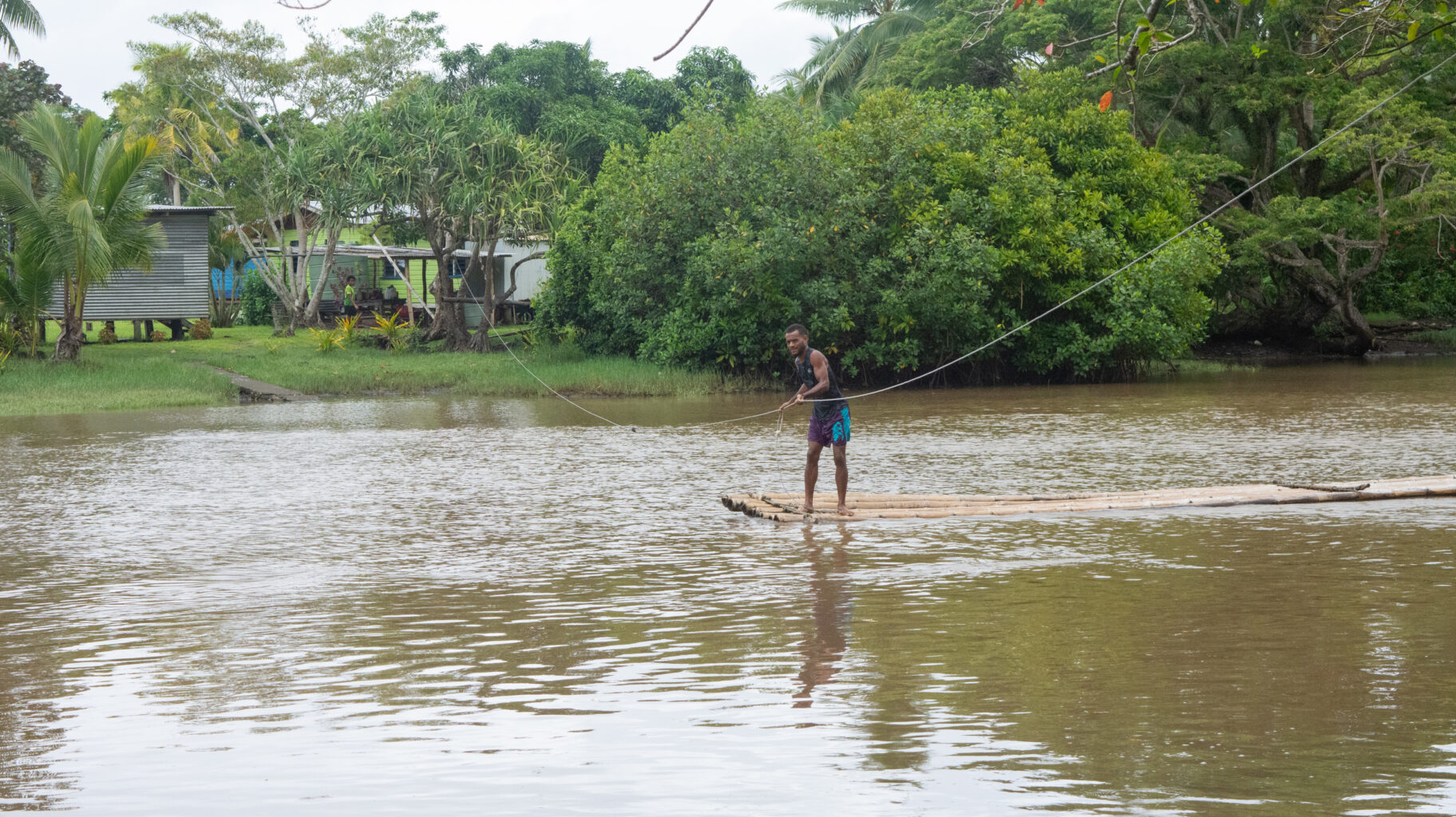 Fijian man pulls bamboo raft across river