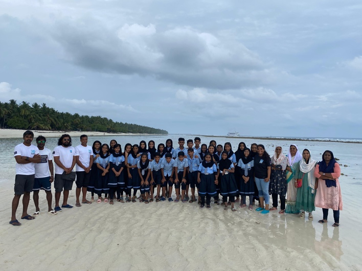 A large group of students and instructors pose on a beach