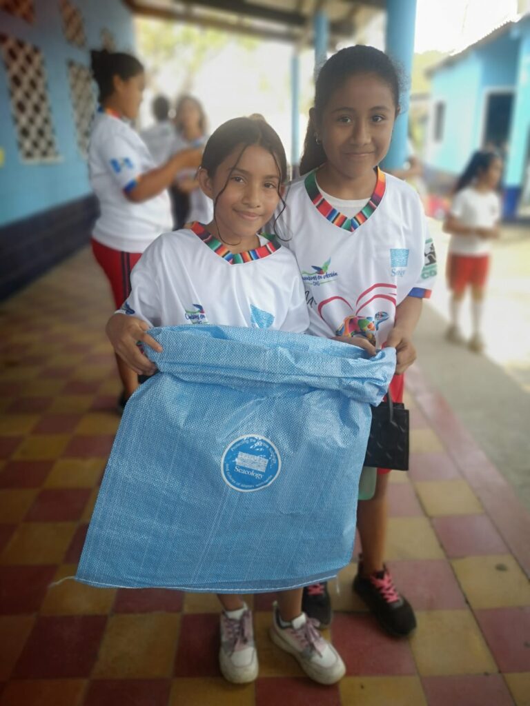 Two children smiling and holding a trash bag