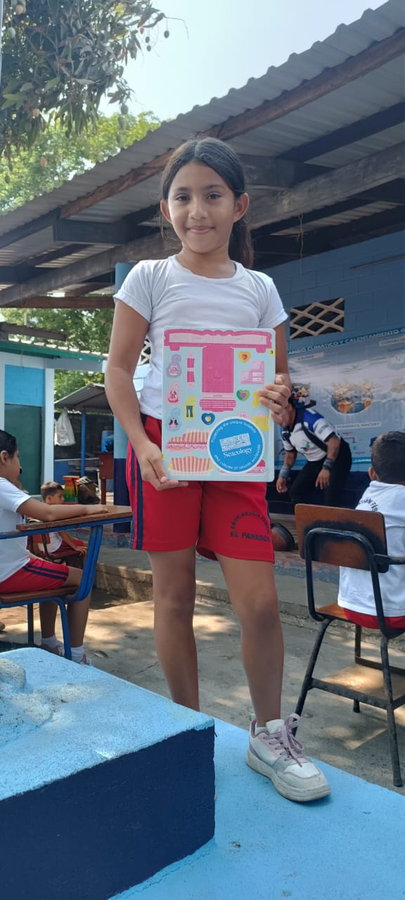 A girl stands on a table holding a book with a Seacology sticker on it