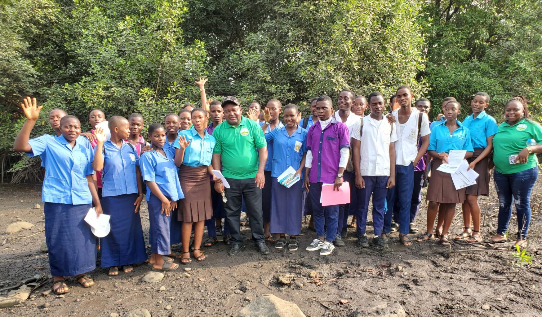 A group of people stands and waves in front of green trees
