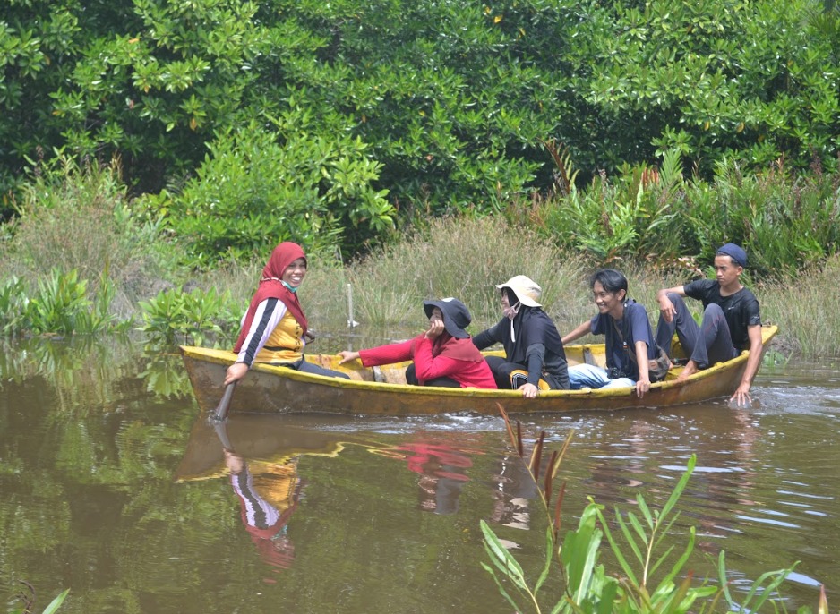 A group of people on a small boat travel along a stream