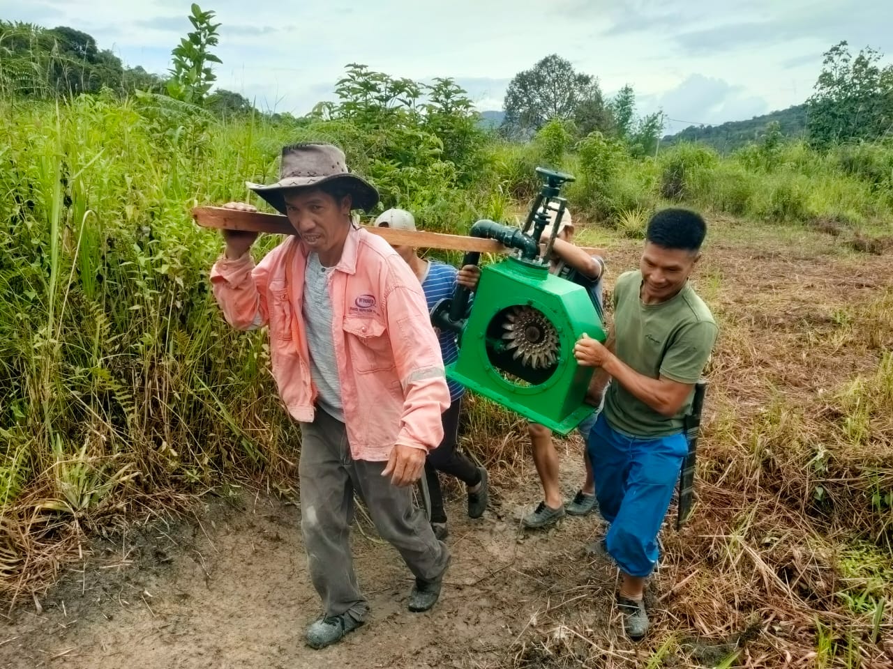 Four people carry the micro-hydro turbine to the project site