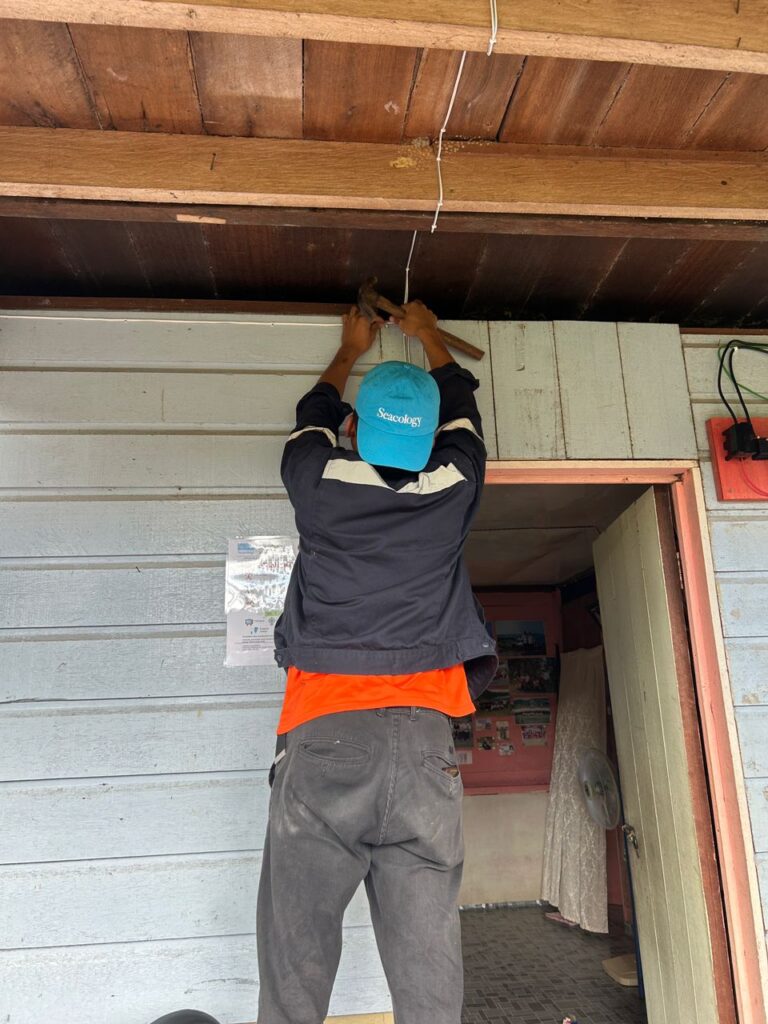 Shot from behind of a man wearing Seacology hat installing electrical wiring