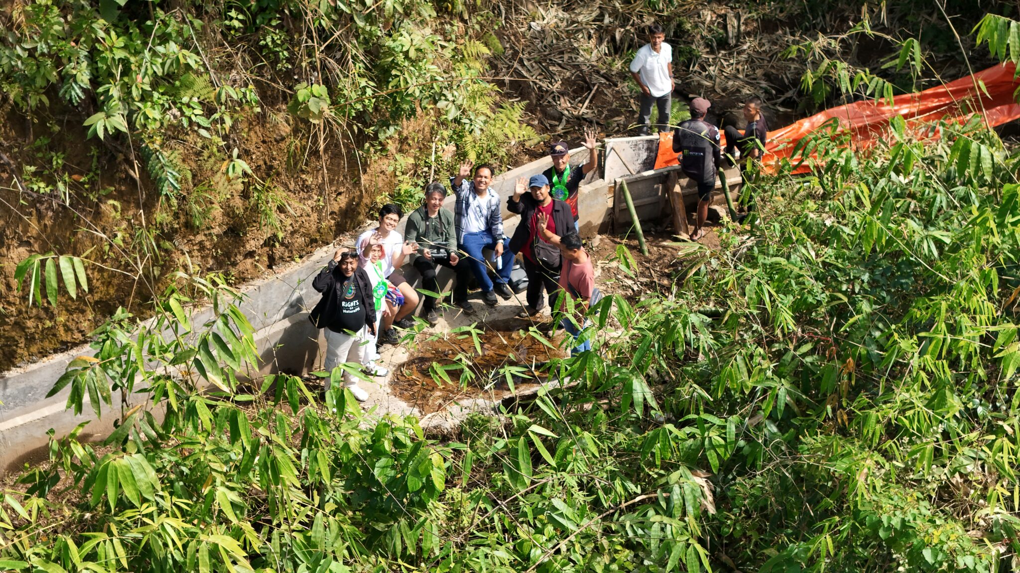 drone shot of a couple of people standing next to concrete water channel, looking up and smiling