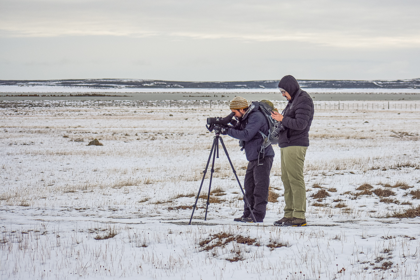 Two people set up a camera on a snowy field
