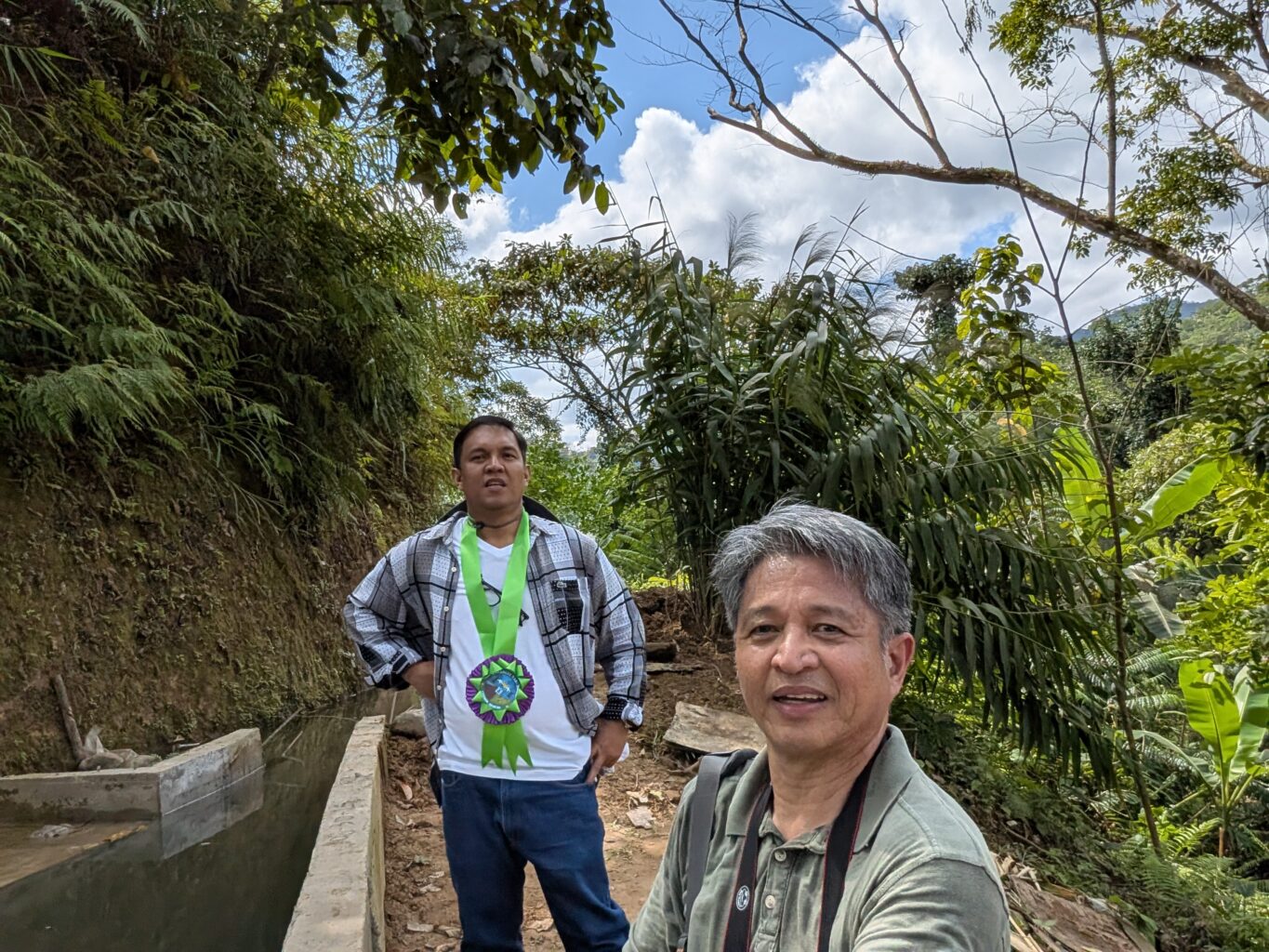 Two men in forest with water channel in background