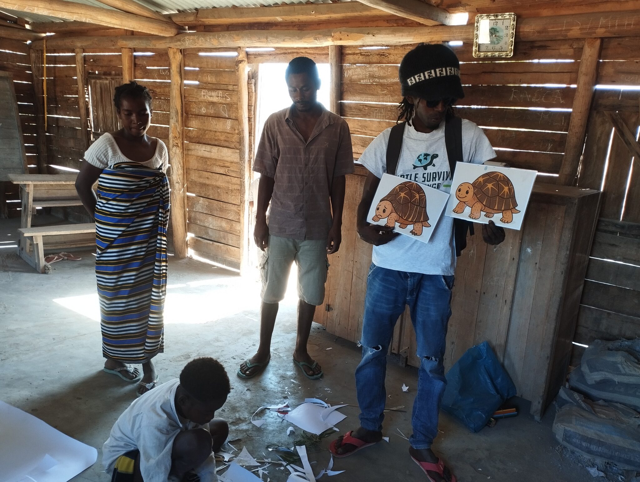 An adult holds up drawings of turtles while a kid sits on the floor and draws