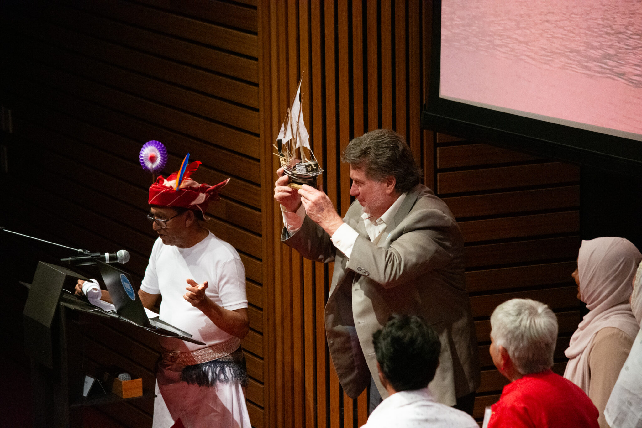 Man holds up model boat to show to audience