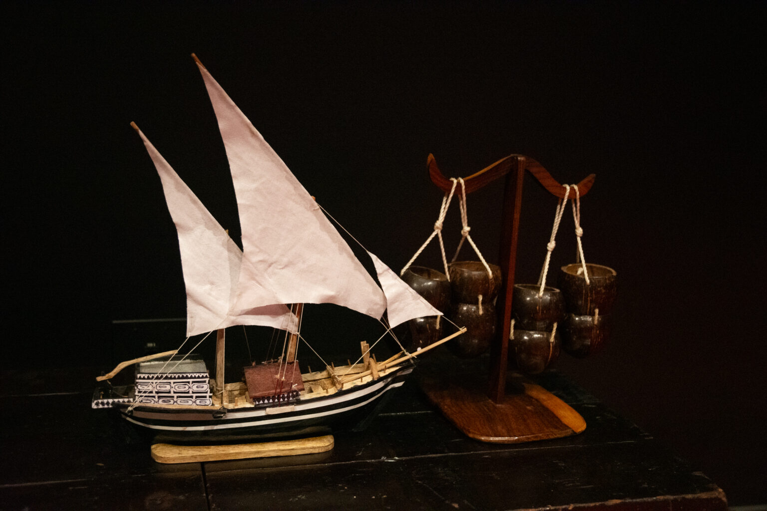 A model boat and device with hanging coconut shells sit on a table