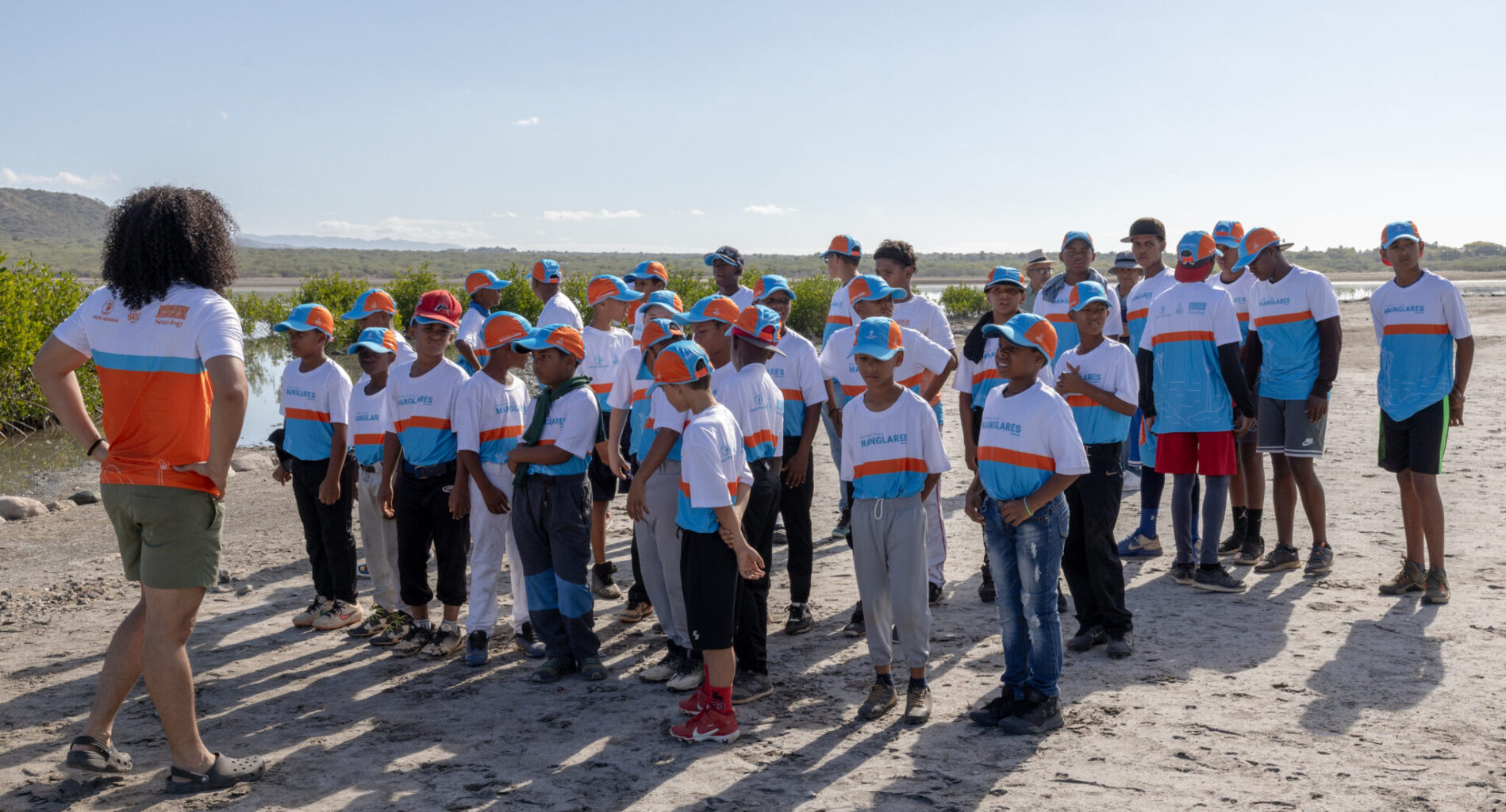 Group of young baseball players listen to coach on beach