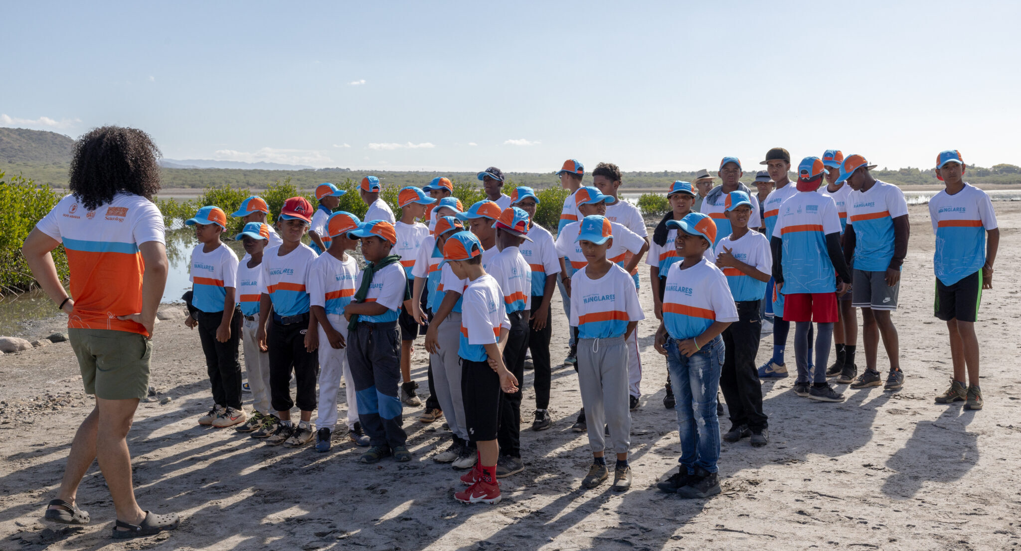 Group of young baseball players listen to coach on beach