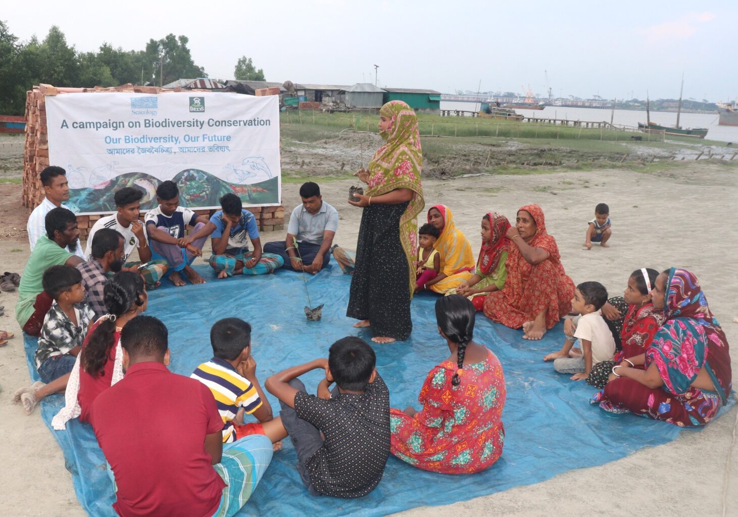 Group of people sitting on ground outside and watch presentation