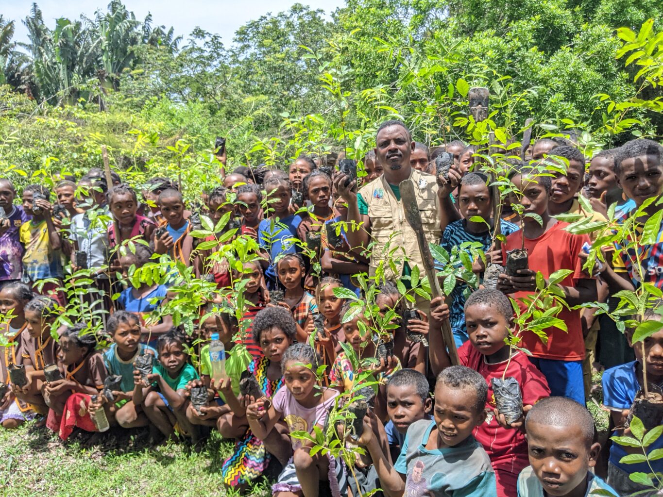 Large group of people, mostly children, holding seedlings to plant