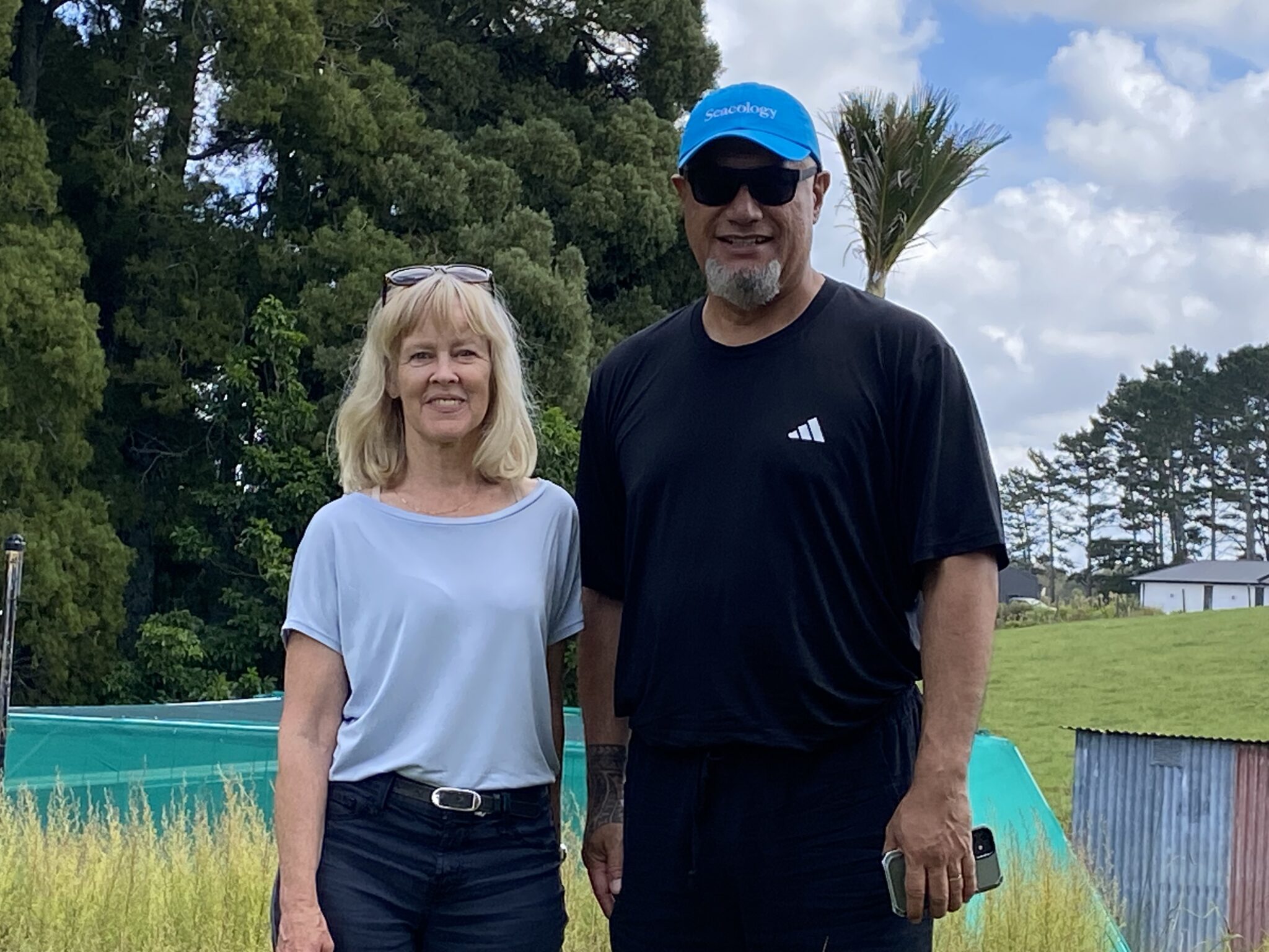 Two people stand and smile at the camera in front of trees