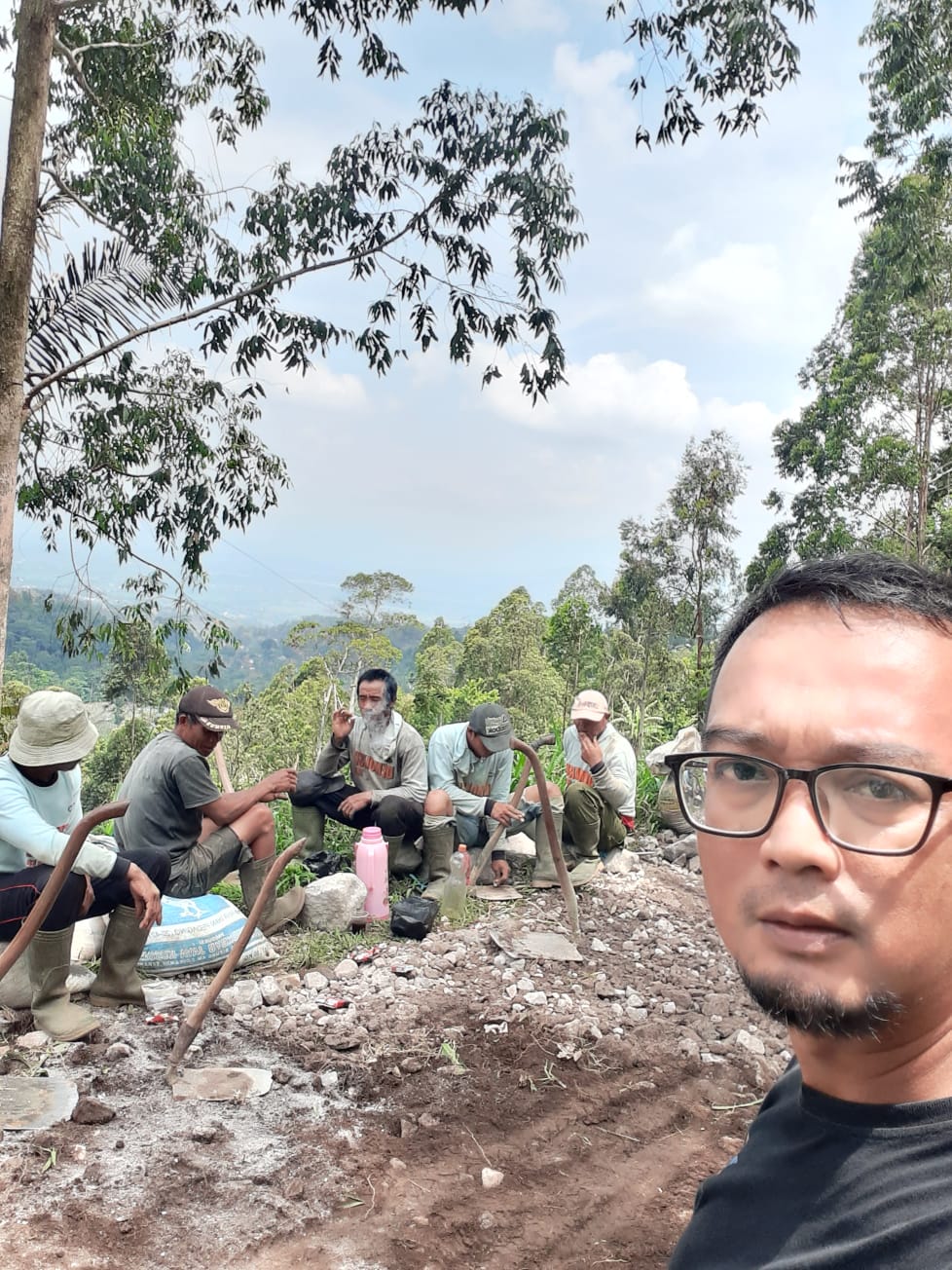 A group of people sit on a rock overlooking a forested valley