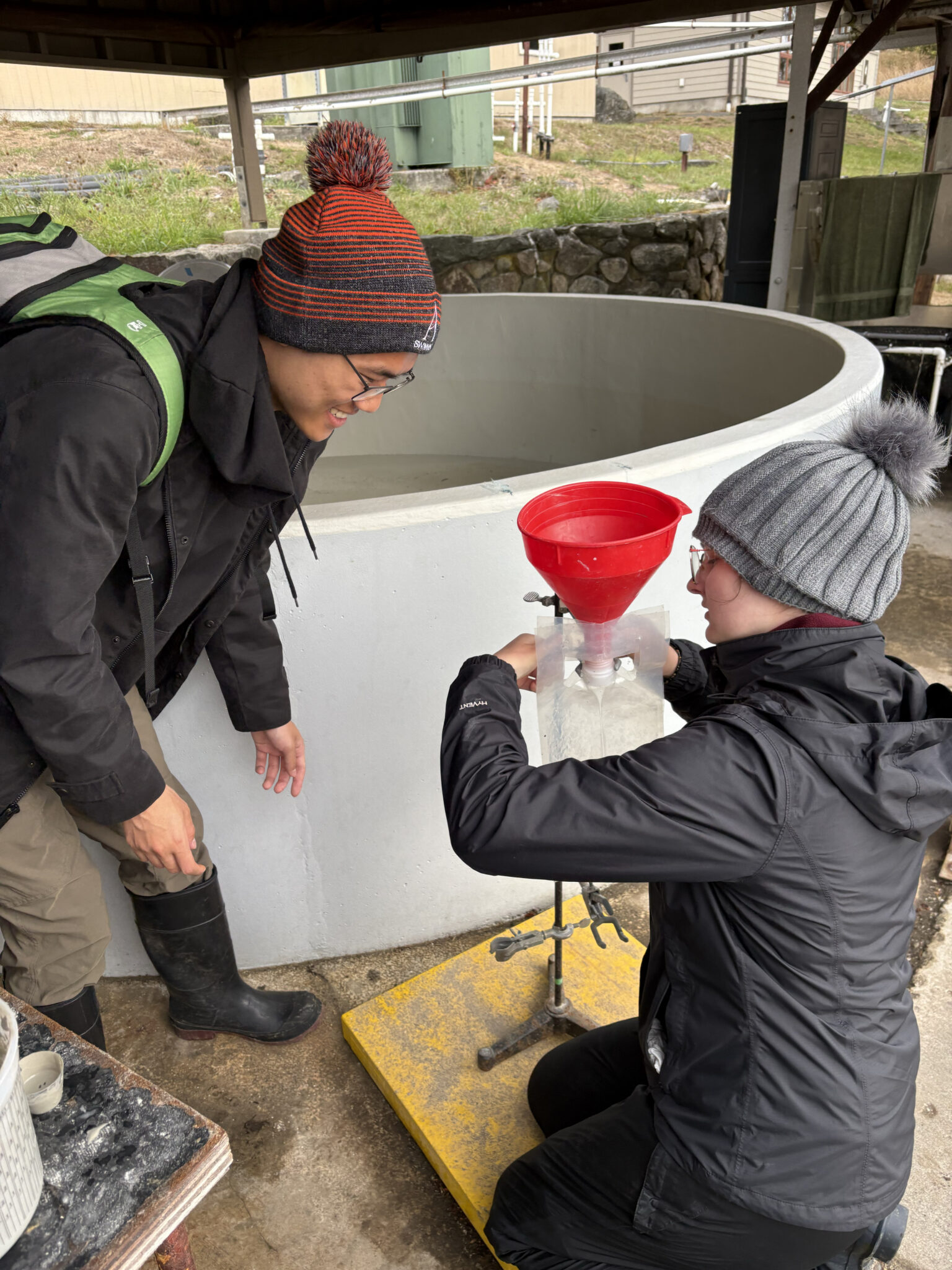 Two teenagers or young adults use a funnel in an outdoor laboratory