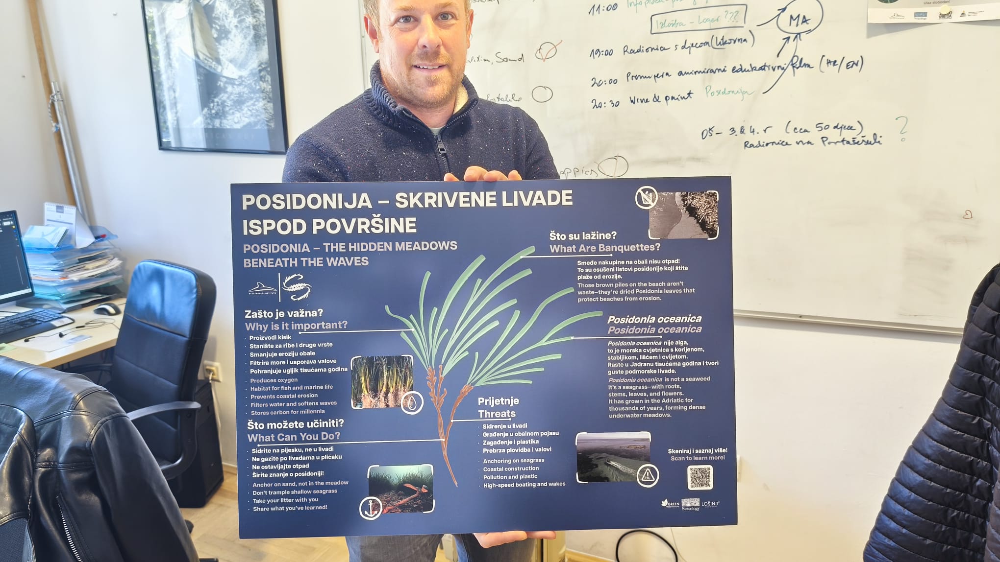 A person holds up a large sign with information about seagrass