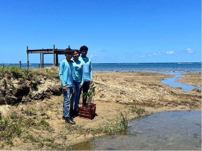 Three students smile together on a beach