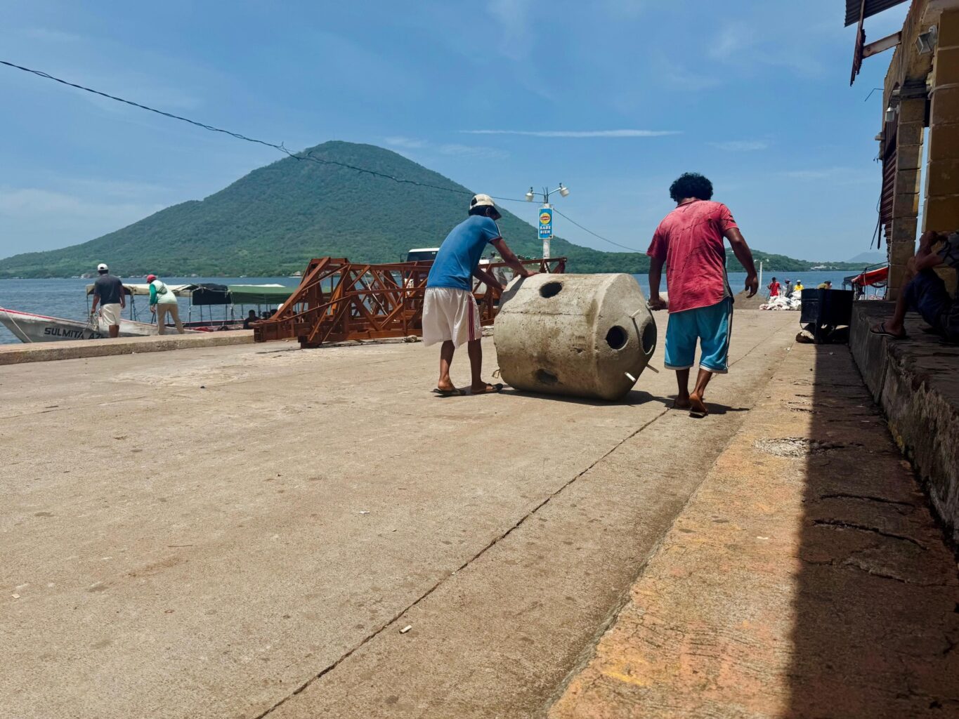 Two people roll a large concrete structure down a pier