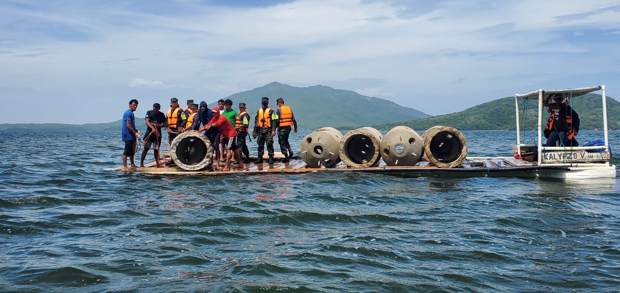A group of people in life vests on a barge prepare large dome structures to go in the water