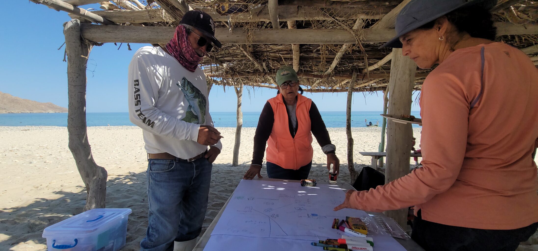 Several people lean over a piece of paper on a table at the beach