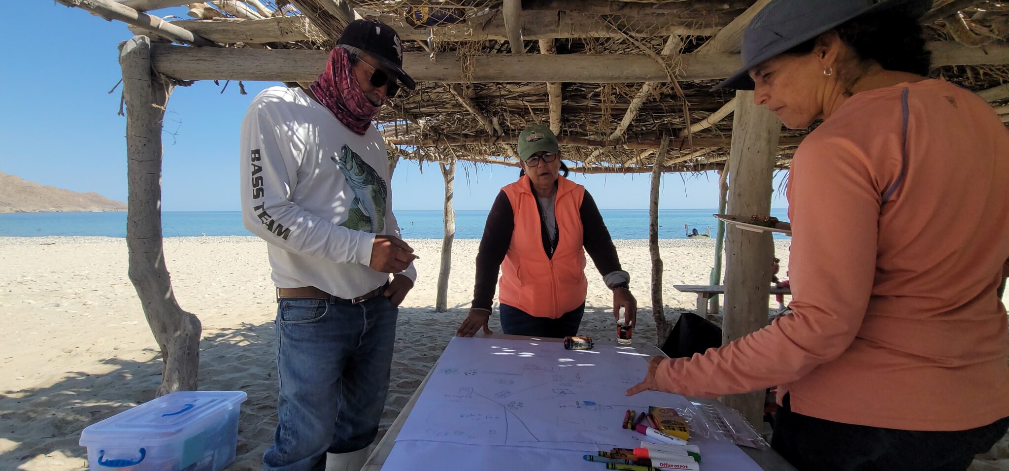 Several people lean over a piece of paper on a table at the beach