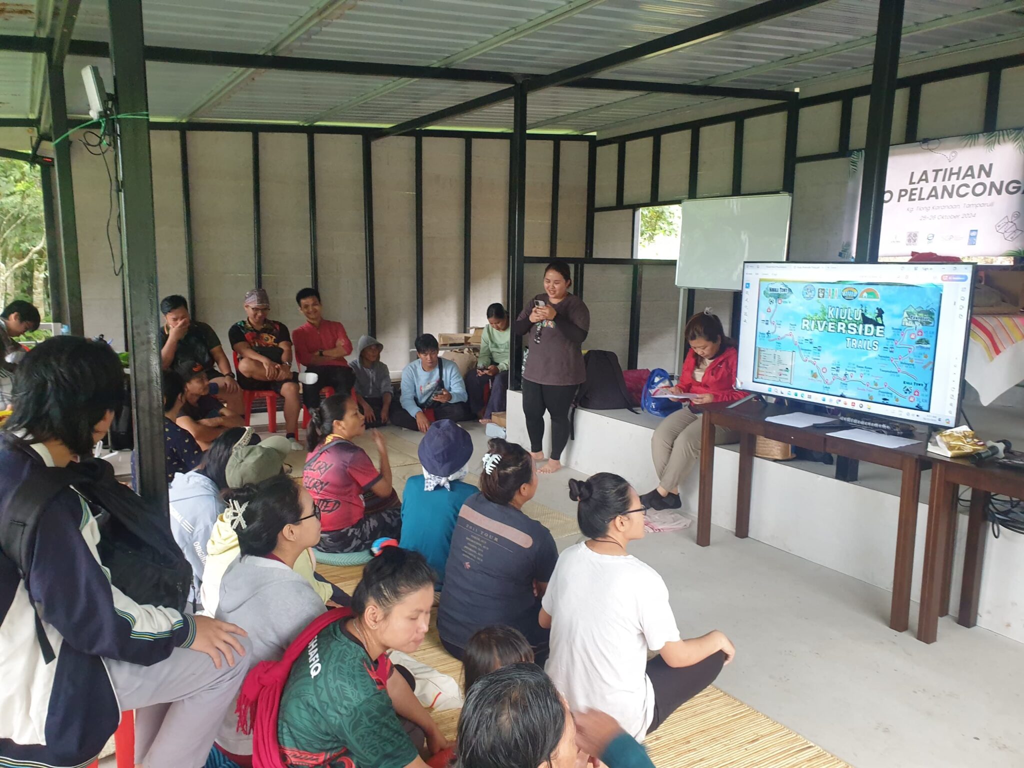 A person presents in a building to a group of people sitting on mats on the floor