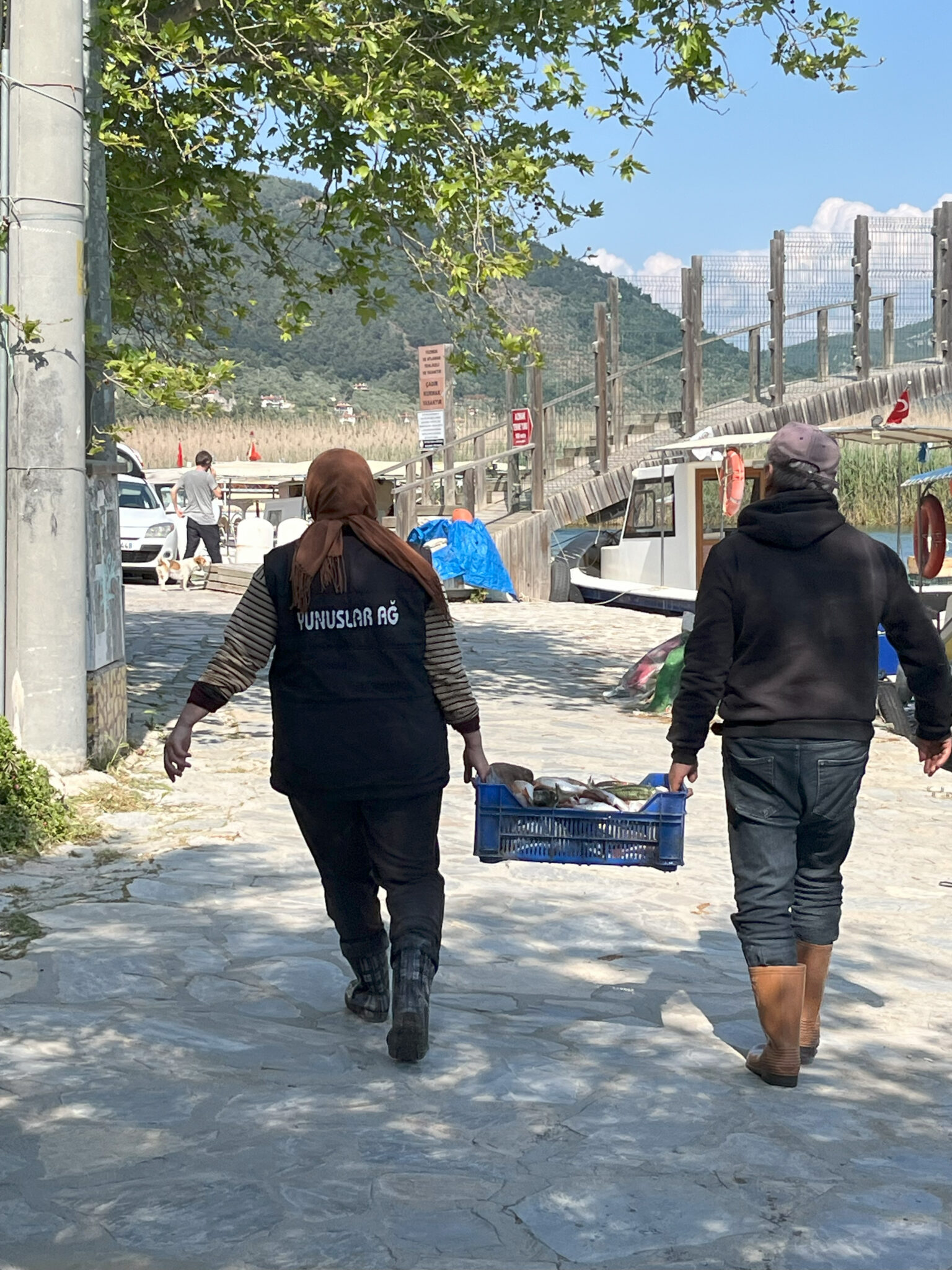 Two people carry a bucket of fish down a street