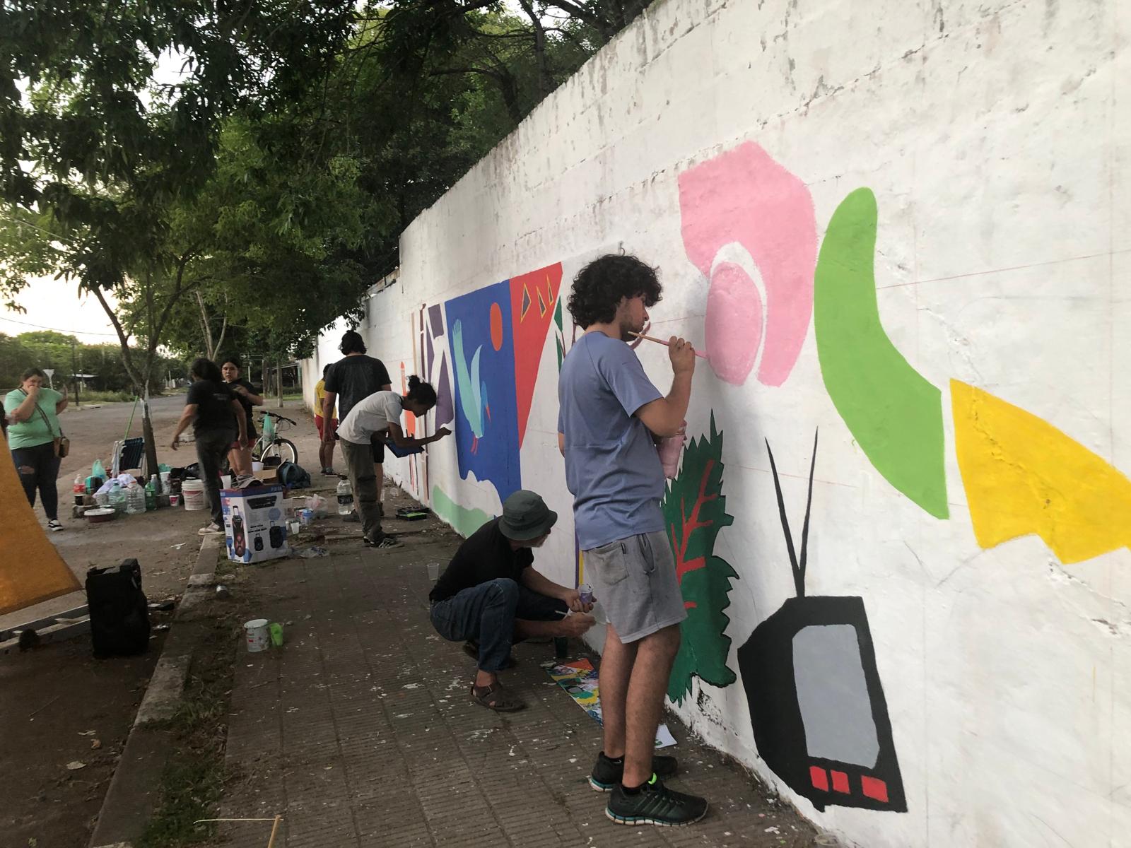 Several people work on painting a colorful mural on a white wall