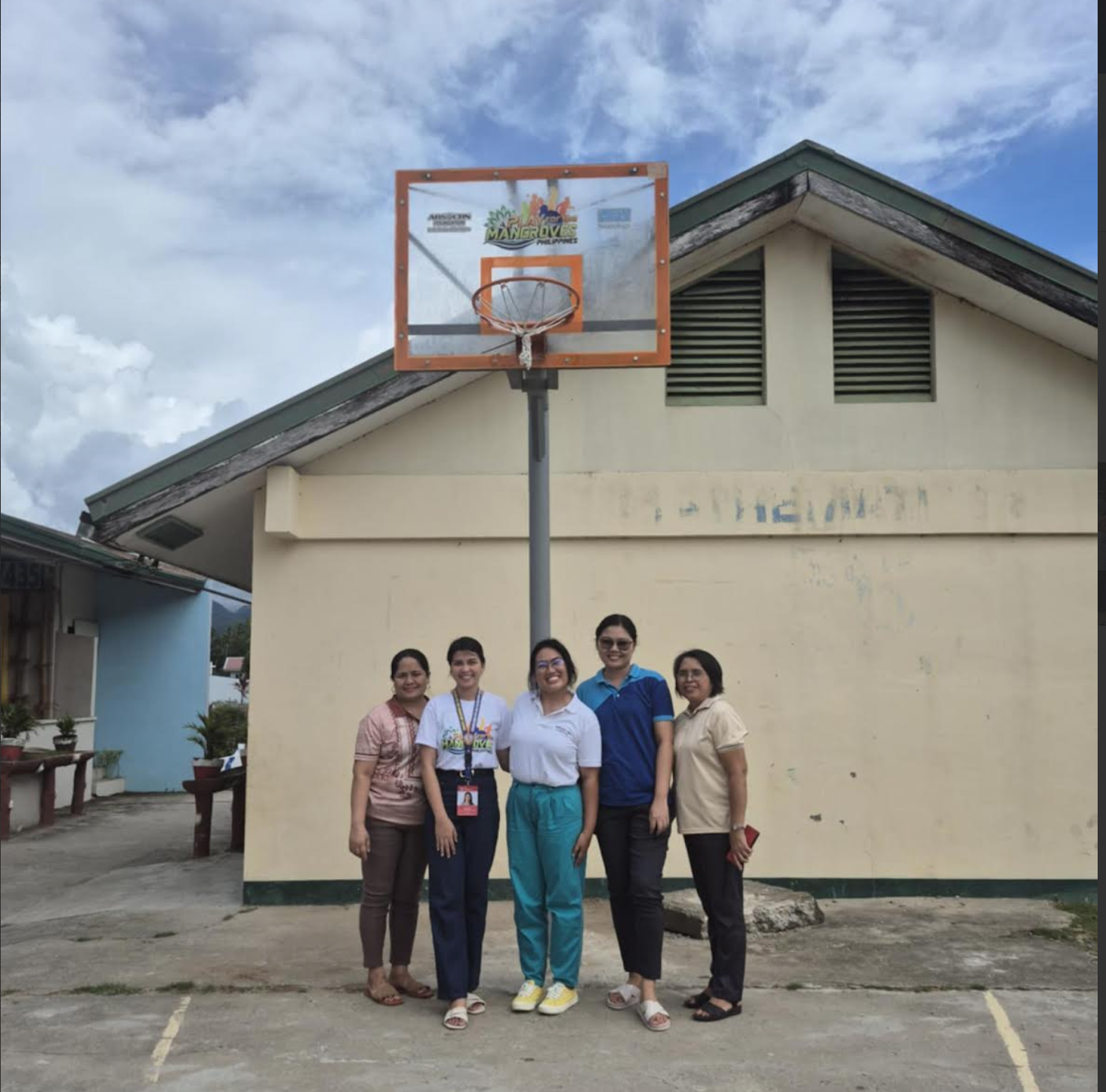 5 people stand and smile beneath a basketball hoop and backboard