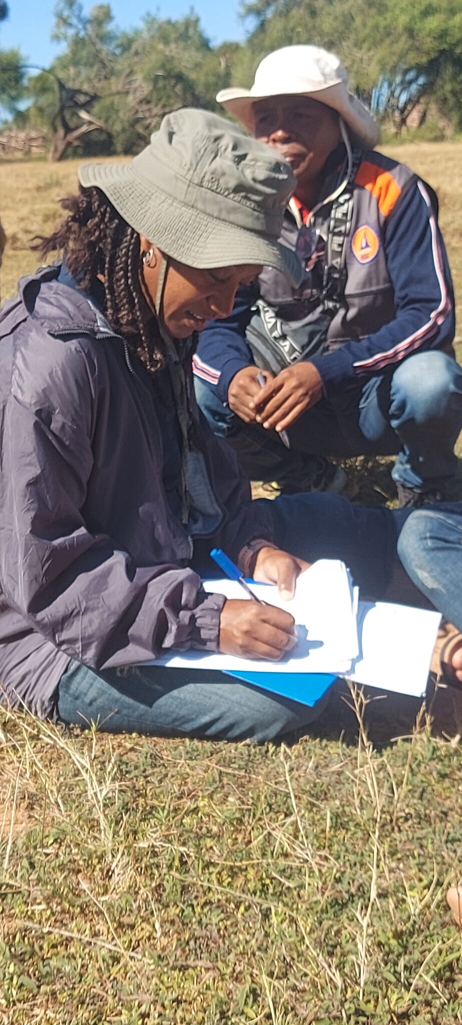 A person sits on the ground and signs a paper