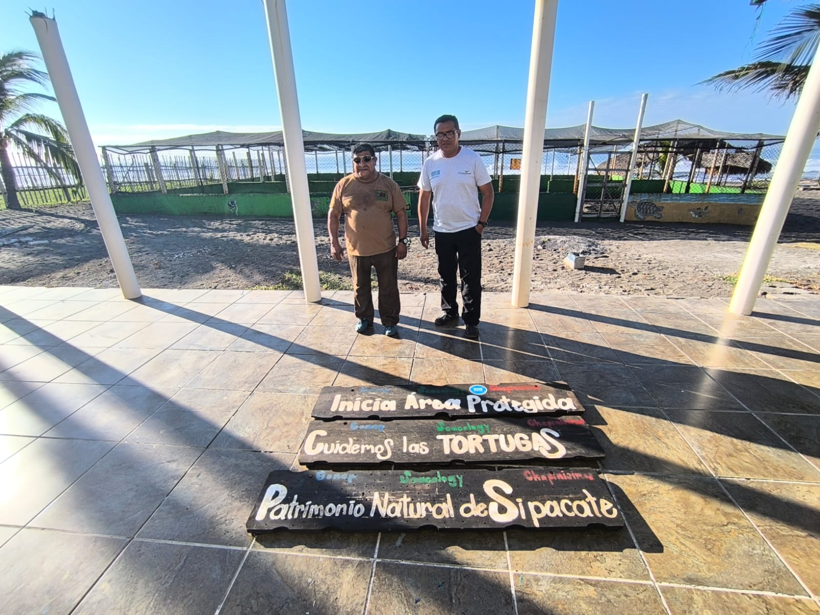 Two people stand on a tile floor with painted signs in front of a turtle hatchery