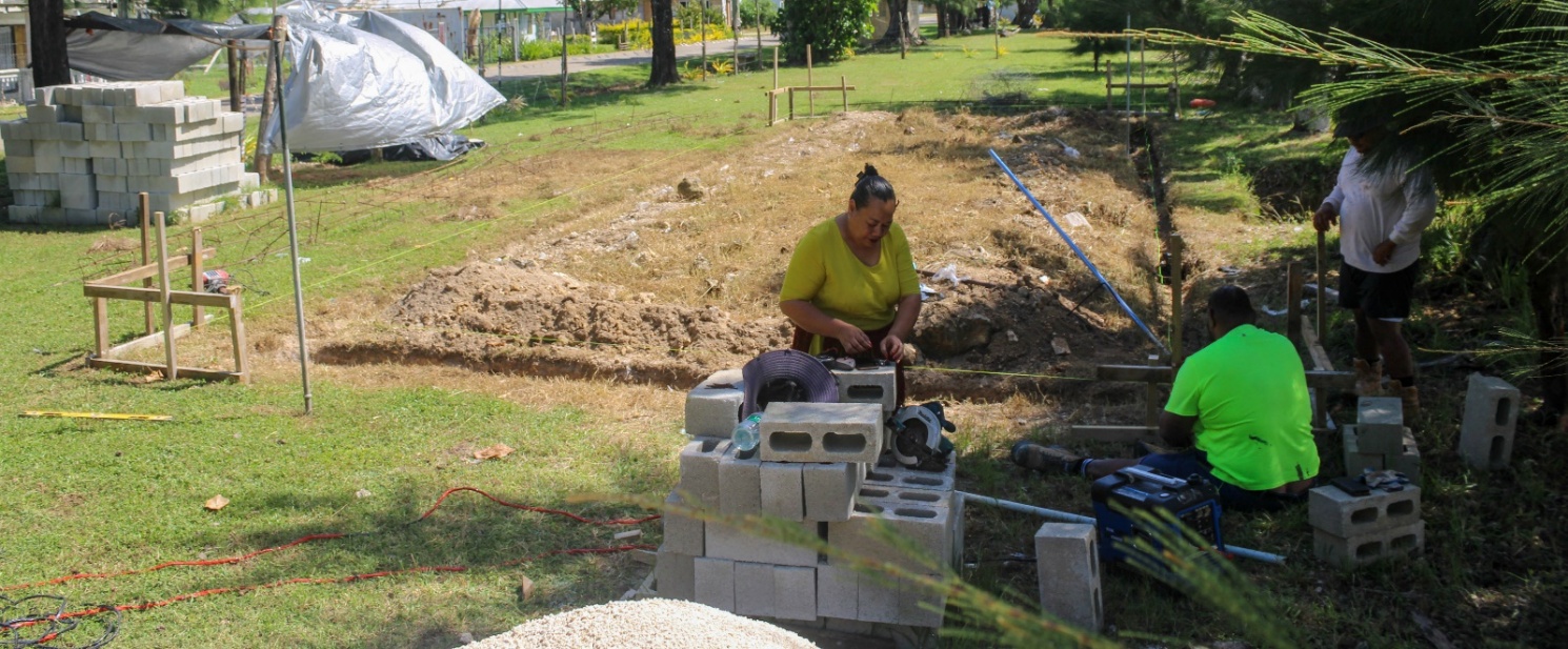 A few people work with piles of cinderblocks on a construction site