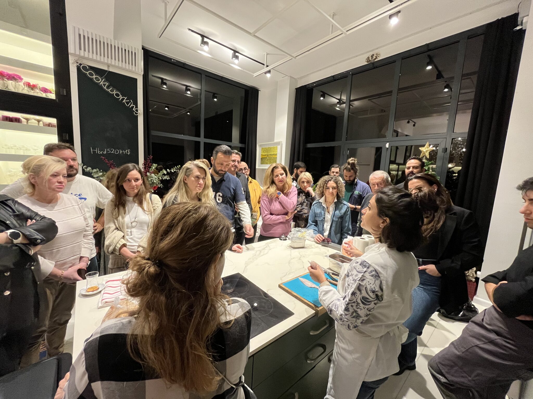 A group of people around a kitchen island watching a chef filet a fish