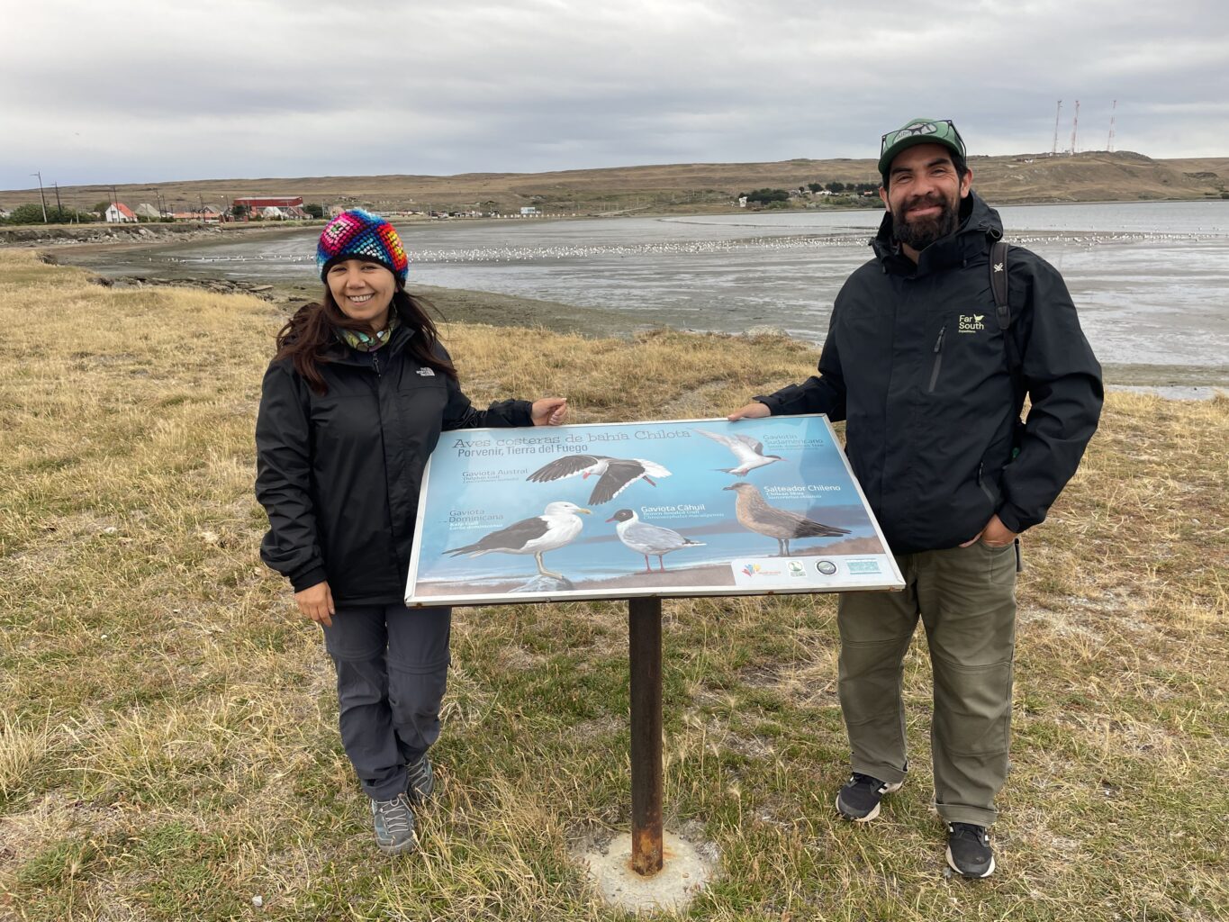 Two people smile next to an informational sign about birds