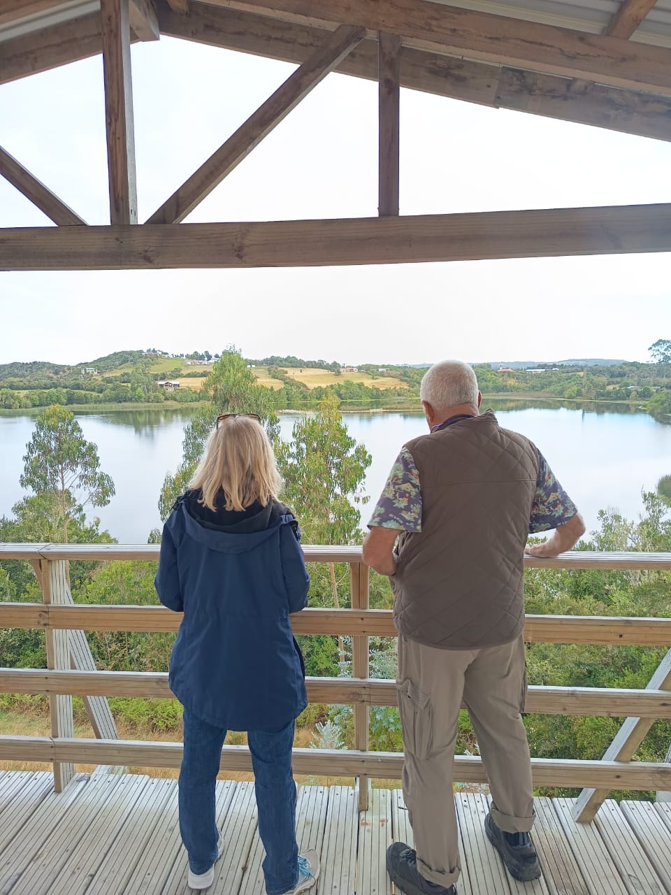 Two people look out over a vista of water and hills from a viewing platform